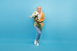 Full length photo of millennial blond funky lady hold flowers wear shirt jeans sneakers isolated on blue background
