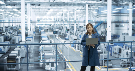 Aufkleber - Shot in an Electronics Factory. Japanese Project Manager Working on Laptop at a Futuristic Industrial Manufacture with AI Robotic Arms. Specialist Monitoring Production on a Computer