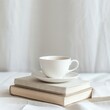 a white coffee cup and book on a table against a white background with natural light, soft tones, a closeup composition,