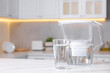 Water filter jug and glass on white marble table in kitchen, closeup. Space for text