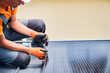 Worker building photovoltaic solar panel system on rooftop of house. Close up of man engineer in gloves installing solar module with help of hex key outdoors. Renewable energy generation concept.