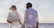 Image of light spots over african american bride and groom holding hands on beach at wedding