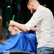 Barber using comb and shaver to cut hair. Professional hairdresser shaving little kid's nape.
