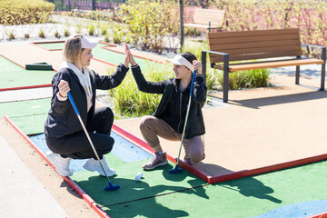 Wall Mural - mother and daughter playing mini golf, children enjoying summer vacation