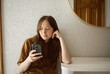 Woman sits by entry way table while scrolling on phone