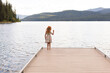 Redhead girl standing on a dock throwing rock into a lake.