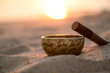 Tibetan singing bowl with stick on seashore on beautiful sunset