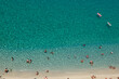 Aerial view of sandy beach with swimming people in sea with transparent blue water in summer.