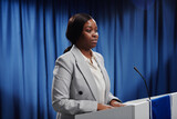 Fototapeta  - Young African American female politician in formalwear keeping her hands on platform while looking at public and speaking in microphone
