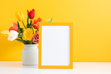 Wall Mural - festive floral background. beautiful tulip flowers and yellow empty photo frame on yellow background