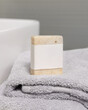 Beige soap bar with a blank label on a gray folded towel near a basin in the bathroom, mockup.
