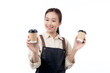 Cheerful young asian woman barista in casual work attire happily holding a takeaway coffee cup, isolated white background, joyful barista presenting takeaway coffee, small business or startup.