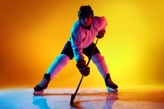 Dynamic portrait of hockey player, poised and ready for action in neon light against yellow gradient background. Concept of professional sport, competition, movement, energy, tournament, match. Ad