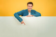 © Jose Calsina - Young caucasian man pointing a blank empty board against red backdrop. Advice copy space mockup. Teenage guy showing a down billboard copyspace at yellow color background wall. Male presenting