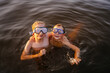Two boys in mask swimming into forest lake at sunset.
