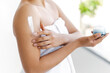 Applying cream. Body skin care routine concept. Close-up photo of a hands of young hispanic or brazilian woman wrapped in a white towel, applying moisturizing cream on the shoulder
