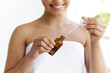 Caring of a body and hands. Vitamin serum in female hands. Skin care concept. Close-up of a smiling hispanic or brazilian woman, wrapped in a white towel, holding hyaluronic serum in her hands