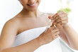 Close-up of a pretty hispanic or brazilian woman, wrapped in a white towel, applying moisturizing serum on her hands after shower, smiling. Caring of a body and hands. Skin care concept