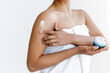 Applying cream. Body skin care routine concept. Close-up photo of a hands of young hispanic or brazilian woman wrapped in a white towel, applying moisturizing cream on the shoulder. Skin hydration