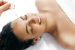 Close-up of a pretty smiling hispanic or brazilian woman, wrapped in a white towel, lying during a procedure with a cosmetologist which applying on her forehead hyaluronic serum. Skin care concept