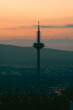 Silhouette of the television tower in the city under the orange sky in the evening