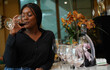 Black female tourist sits holding a glass of red mattos wine, happily tasting wine at the counter bar in a wine shop.