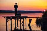 Fototapeta Sypialnia - Amazing sunset over calm lake with fisherman catching fish.