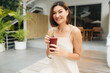 Attractive asian woman in a beige dress with a berry smoothie is standing outdoors