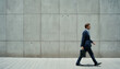 © Sergiy - Business person, businessman walking on the background of concrete gray wall blurred in motion. The concept of the modern fast pace of life