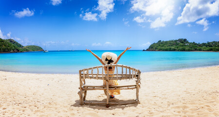 Wall Mural - a woman with sunhat sits on a driftwood bench at the tropical carlisle bay beach, antigua and barbud