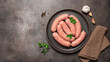 Raw sausages in a plate on a dark grunge background. Top view, flat lay, banner.