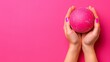   A woman's hands hold a pink ball against a pink backdrop, her nails perfectly painted pink