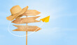 wooden road sign with a beach hat on the edge and a flying paper airplane against the sky. travel concept