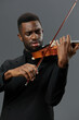 Soulful African American man playing the violin in elegant black suit on neutral gray background