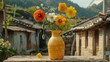   A yellow vase, brimming with an abundance of flowers, sits atop a weathered wooden table Beyond the scene lies a structure, framed by towering mountains in the distance