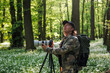 Wildlife photographer is bird watching in forest. Man with camera on tripod is looking for birds in spring woodland