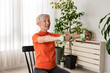 Smiling beautiful senior woman health instructor doing chair exercises with dumbbells