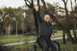 Man Waving Hello While Standing Next to Bike in a Park