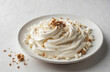 A white plate with a white creamy dessert and some nuts on top