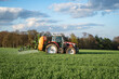 Getreideanbau - roter Traktor mit angebauter Feldspritze bei einer Pflanzenschutzmaßnahme im Getreidefeld.