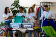 © ArtSys - Group of volunteers, young women and man, sorting clothes in charitable foundation for charity donation, recycling. Concept of textile pollution, conscious consumption. Ecology, sustainable lifestyle