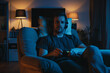 © ADDICTIVE STOCK - AI Generated Image. Serious man relaxing on a chair and playing video game while wearing headphones at night