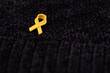 Hands placing a yellow ribbon pin on fabric, the international symbol of advocating for the return of hostages and raising awareness for cancer (specifically sarcoma) support and solidarity.