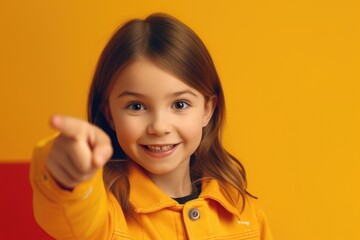 Wall Mural - A young girl in a yellow jacket pointing to something. She is smiling and she is happy