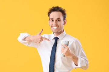 Poster - Young businessman pointing at money on yellow background