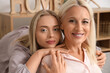 © Pixel-Shot - Happy young beautiful woman with her mother sitting in living room and hugging