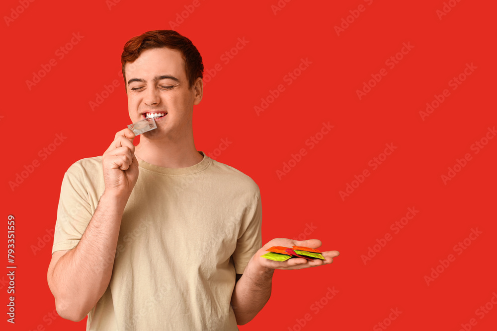 Young man with condoms on red background. Safe sex concept