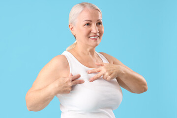 Wall Mural - Mature woman checking her breast on blue background. Cancer awareness concept