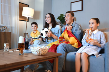 Canvas Print - Happy family with Spanish flags watching football game on sofa at home in evening