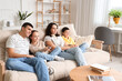 © Pixel-Shot - Happy family watching TV on sofa at home